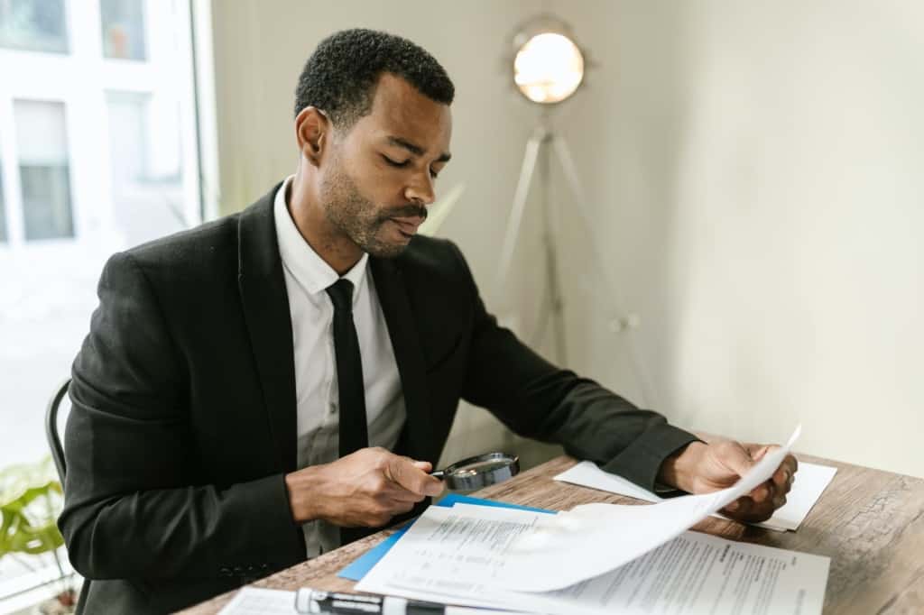 man in black suit jacket holding white paper and black magnifying glass